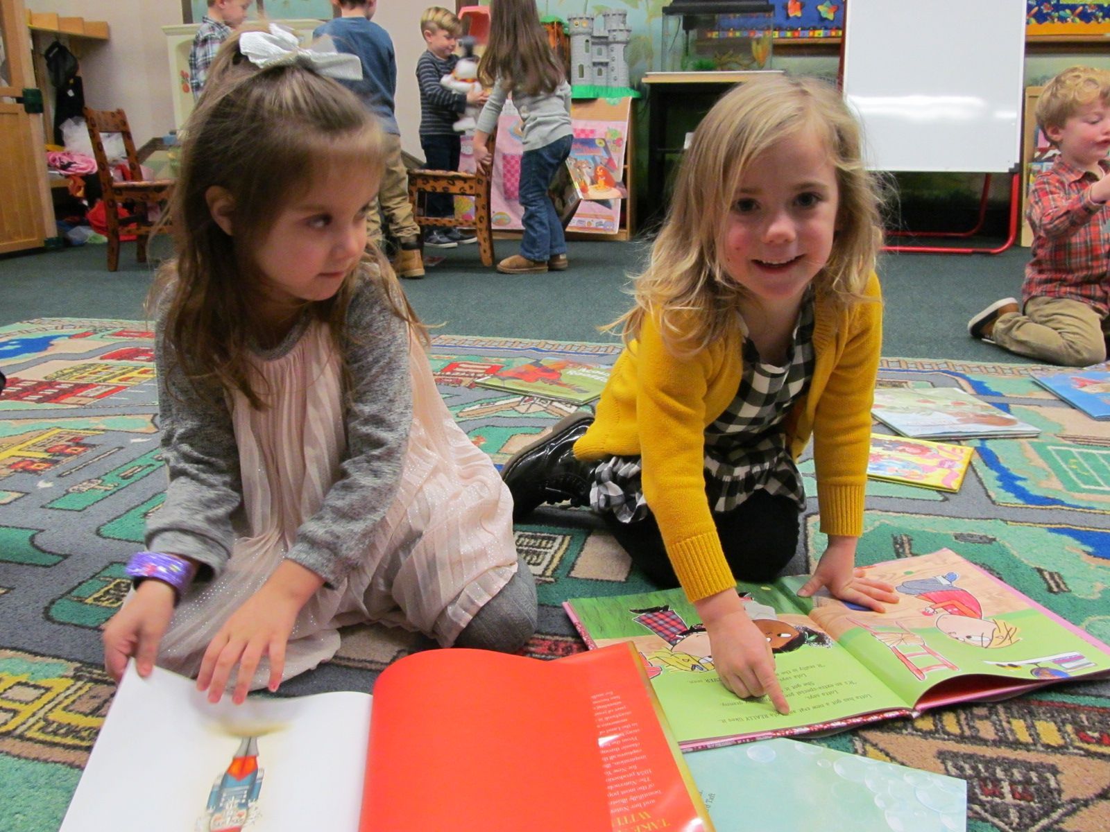 Two children sitting on a classroom rug, looking at books and pages during a reading activity