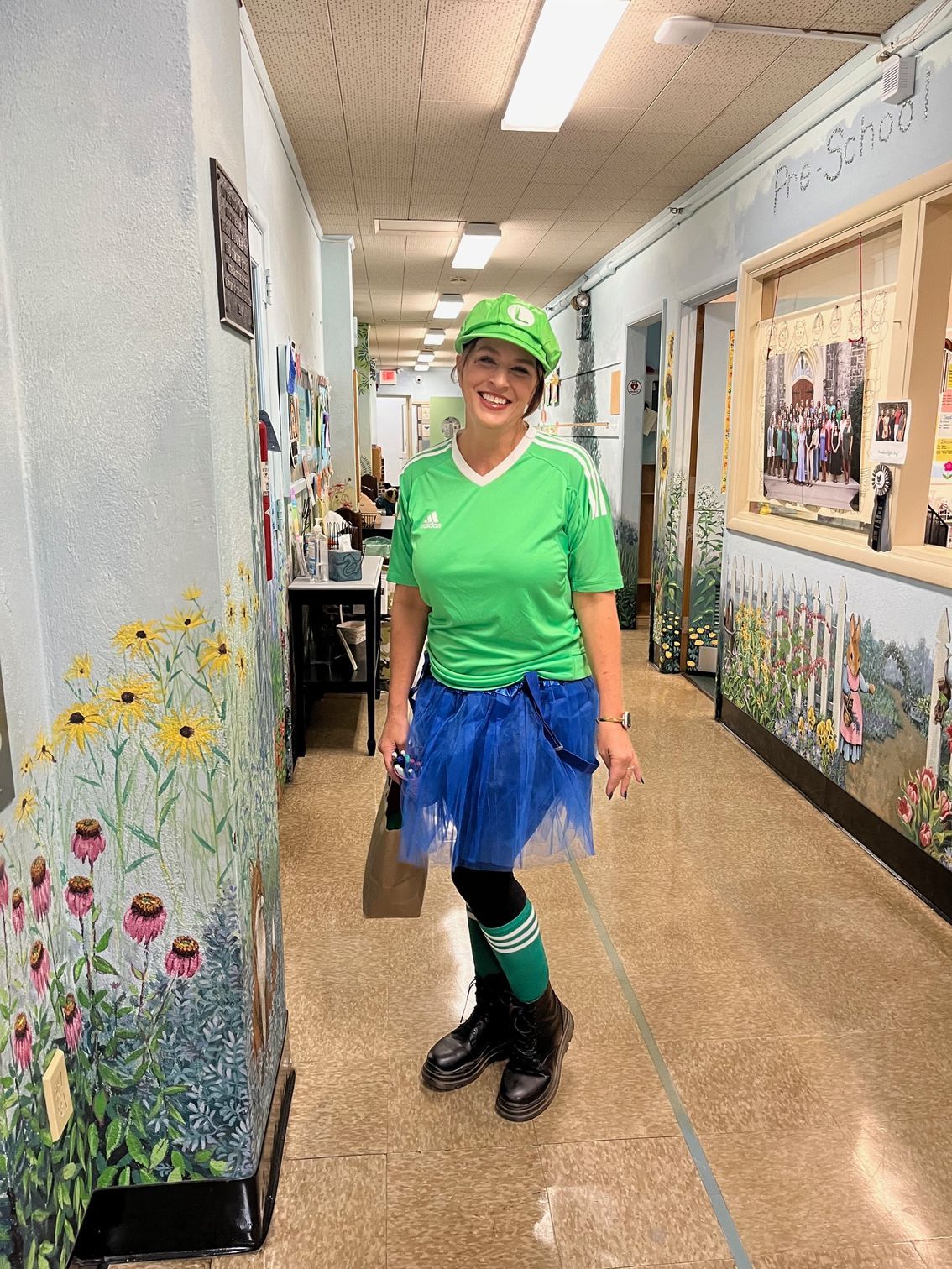 Person in bright green and blue costume standing in a school hallway, smiling.