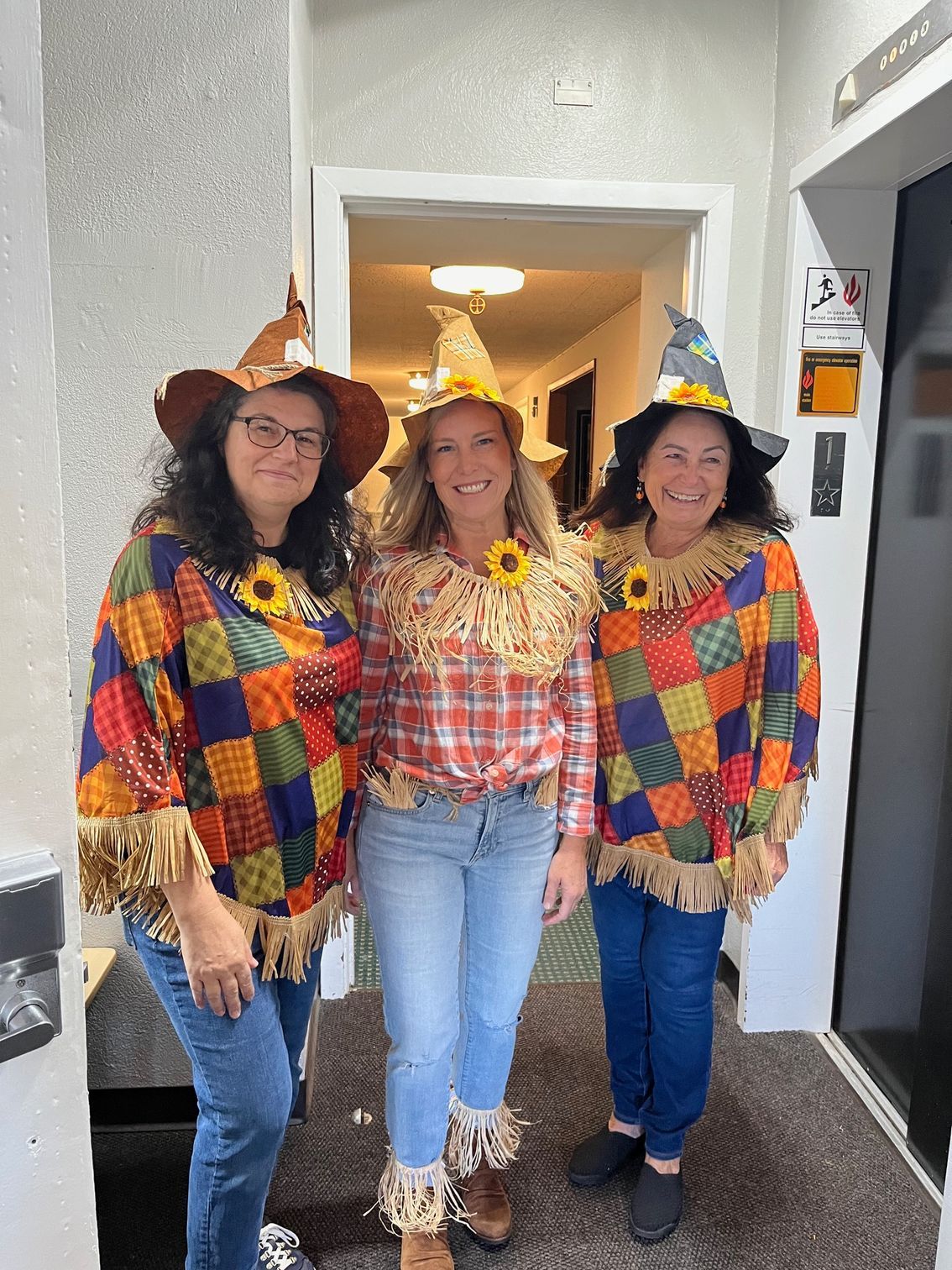 Three people in colorful costumes and party hats standing in a doorway, smiling.