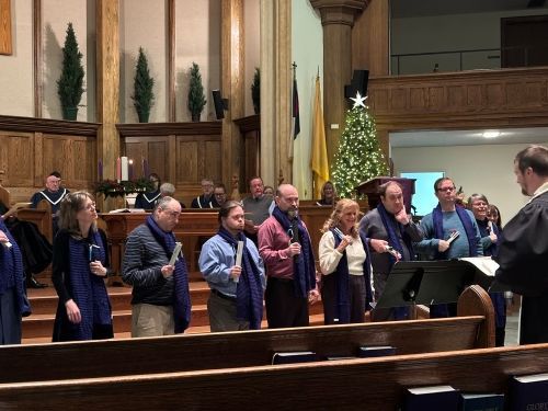 Choir members standing in a church, singing near a Christmas tree and piano