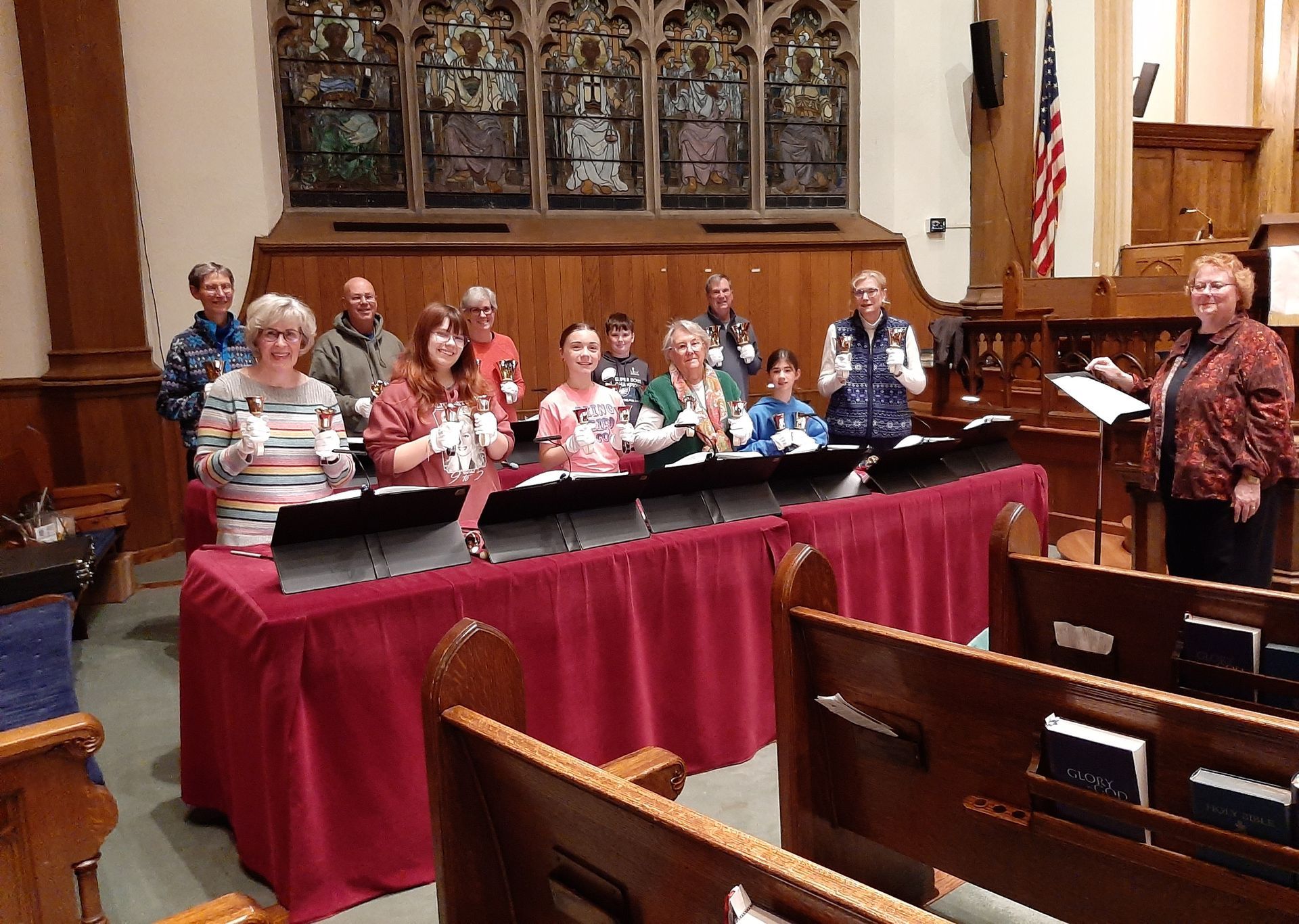 Bell choir standing behind tables in a church, with pews and a carved altar in the background.