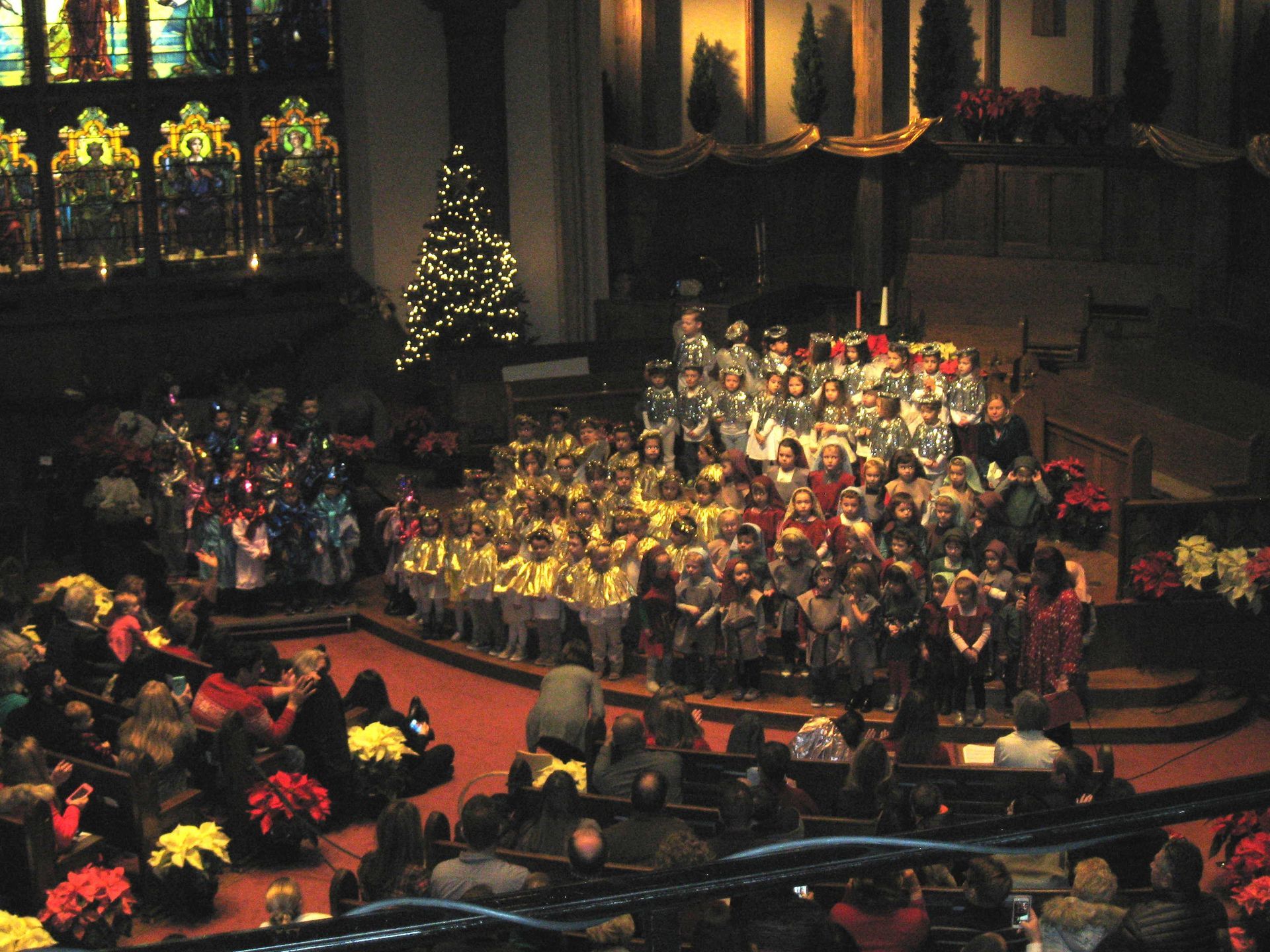 Choir and orchestra performing in a large church, with candles and poinsettias decorating the stage.