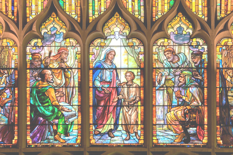 Stained-glass church window showing several biblical figures in colorful robes beneath gothic arches