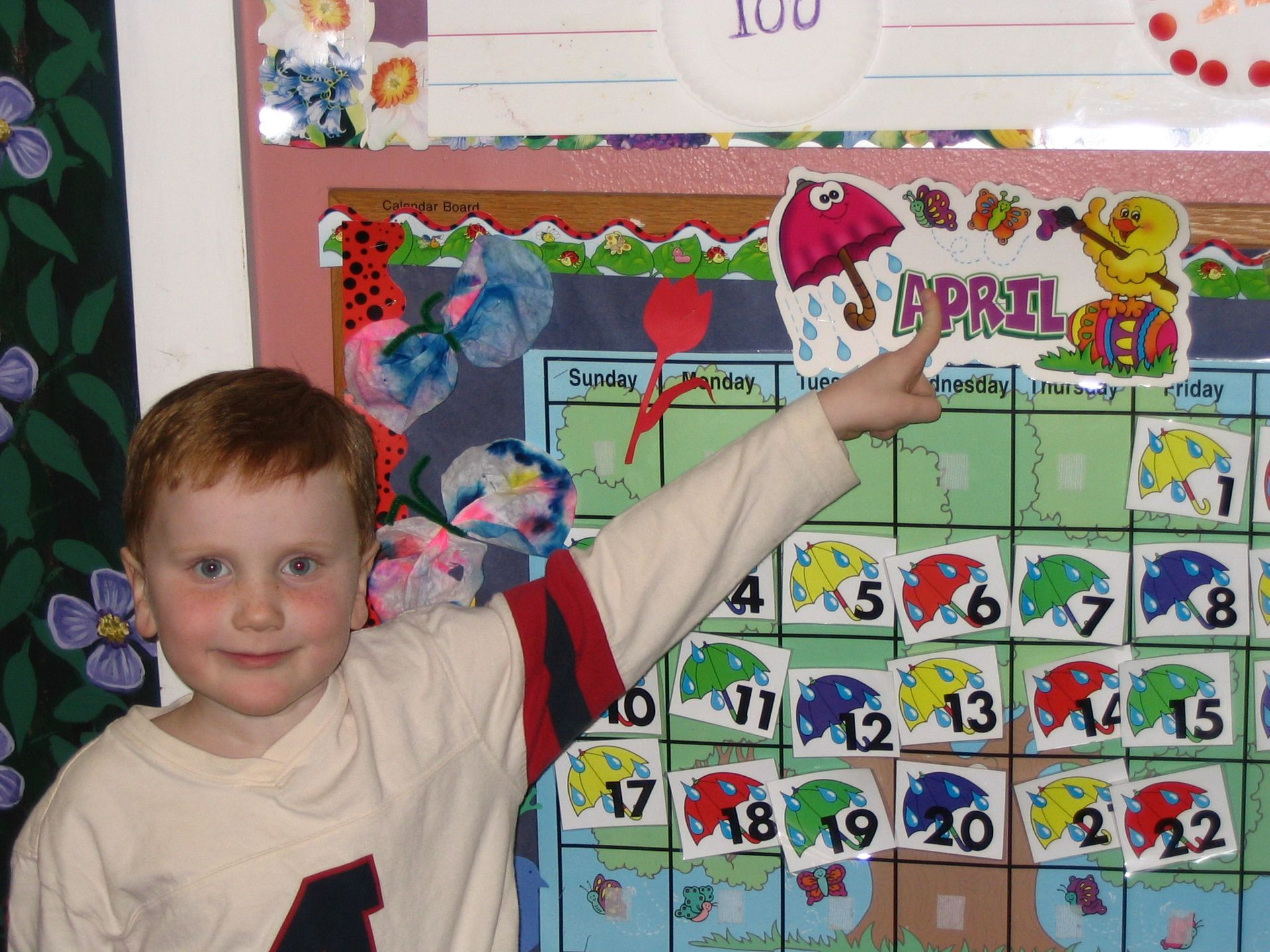Child pointing at a colorful classroom calendar wall with numbers and decorations