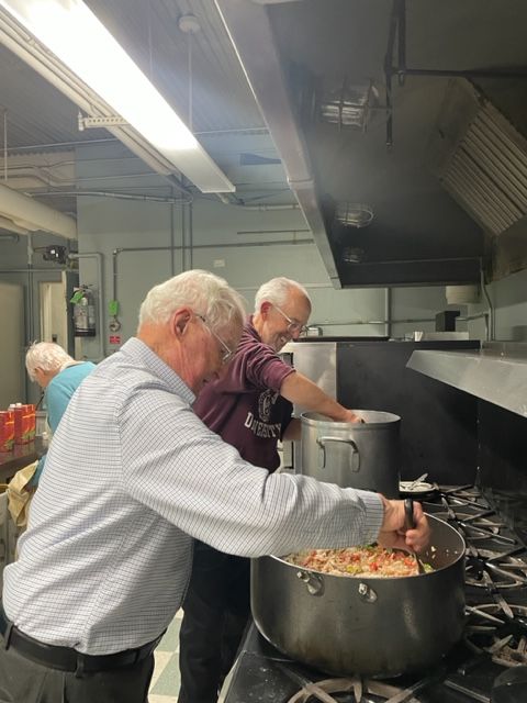 Two people stirring large pots of food in a commercial kitchen
