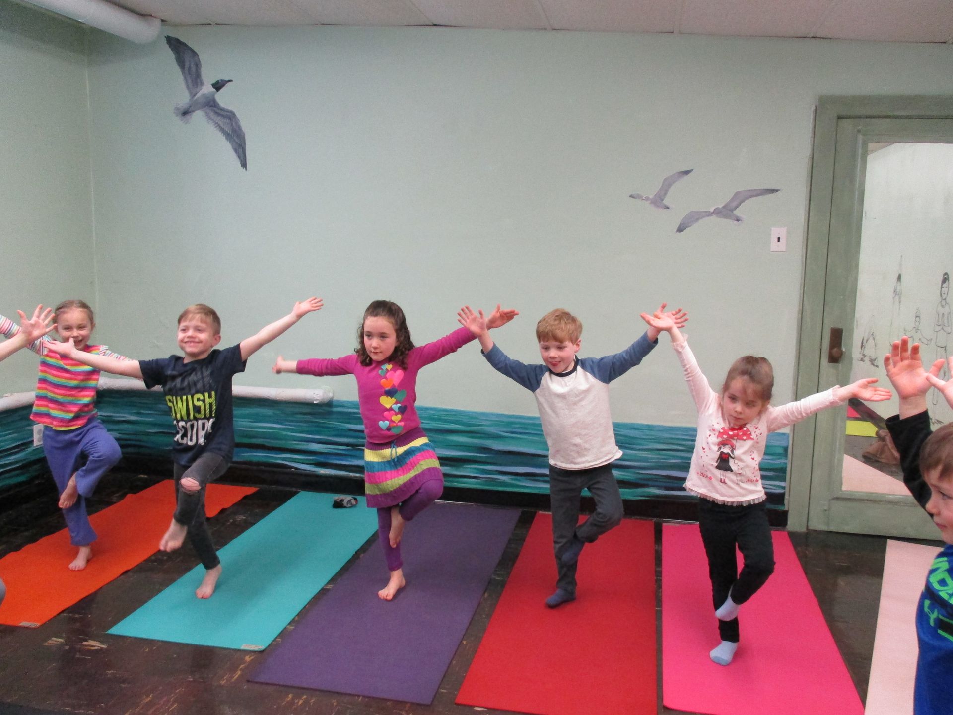 Children doing yoga poses on colorful mats in a room with bird wall art