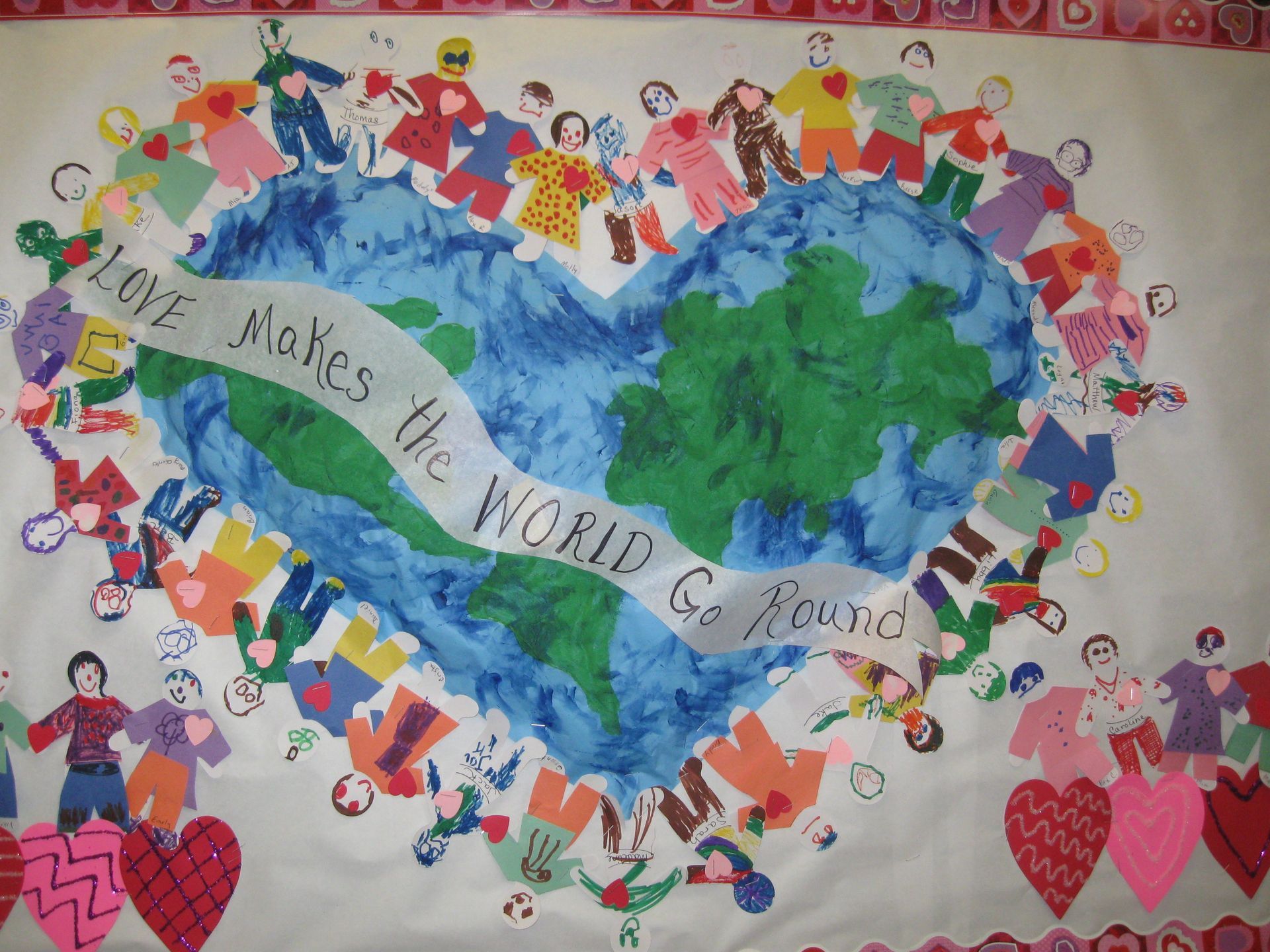 Children's artwork of Earth in a heart, with figures holding hands and a banner reading 