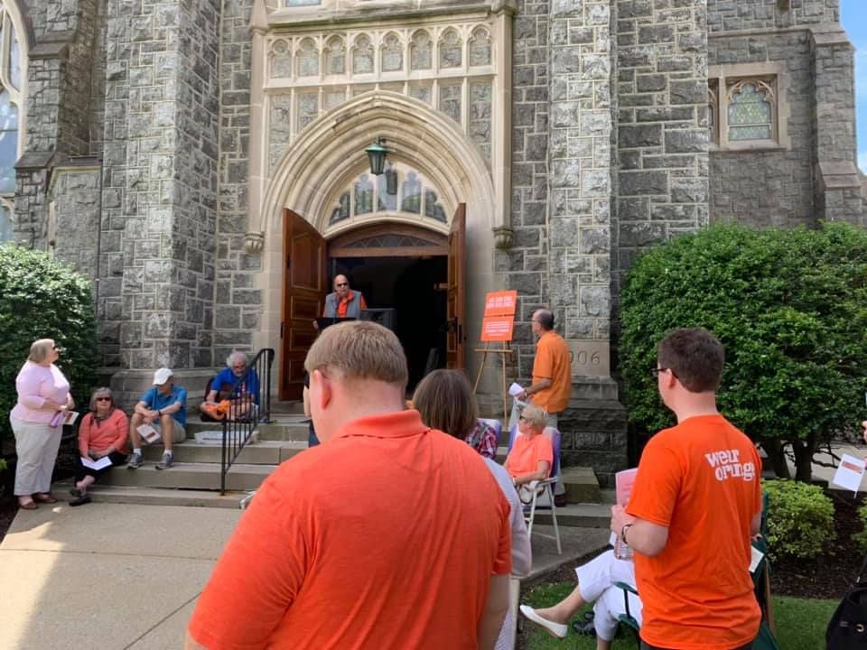People gathered outside a stone church entrance, with two men in orange shirts in the foreground.