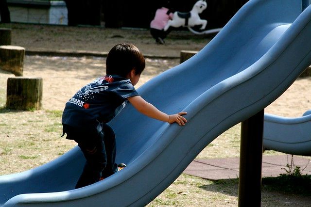 Child climbing a blue playground slide outdoors, with a small dog in the background