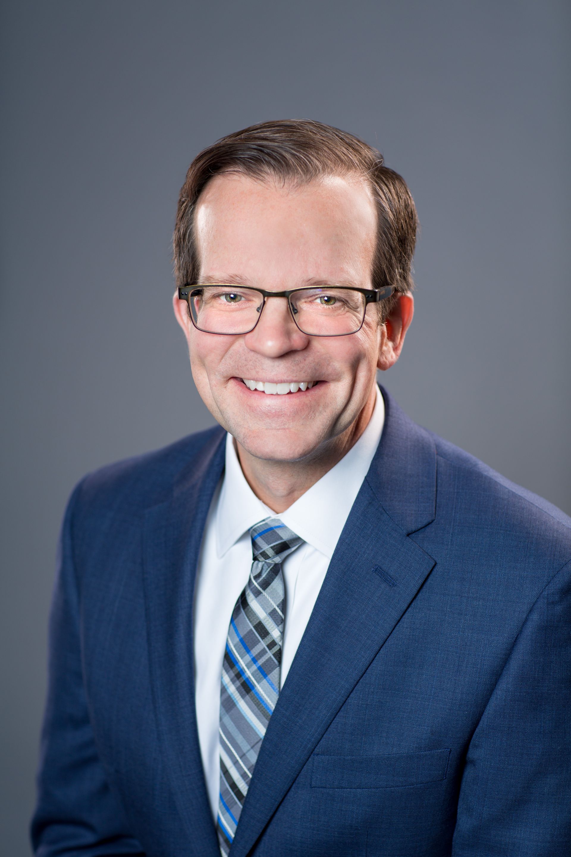Man in a blue suit and plaid tie smiling against a gray studio background