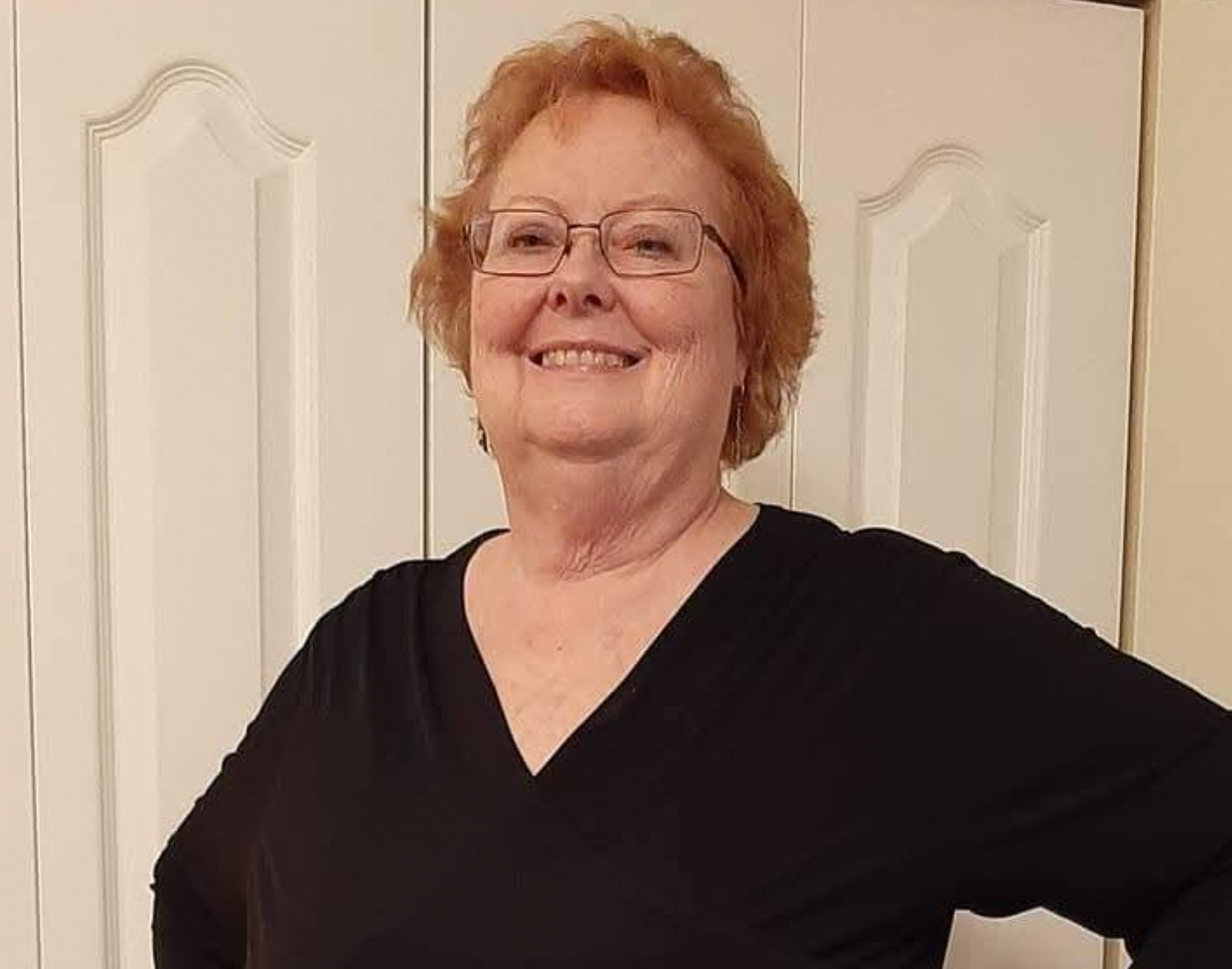 Smiling woman in glasses wearing a black top, standing in front of white closet doors