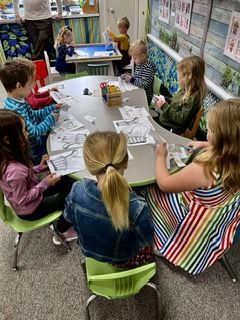 Children seated around a classroom table doing a craft activity with papers and supplies