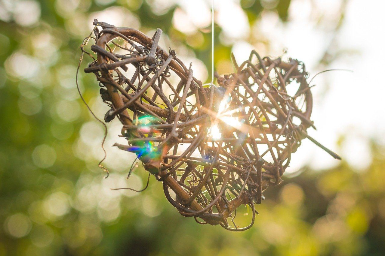 Woven twig heart hanging in sunlight, with soft green bokeh background