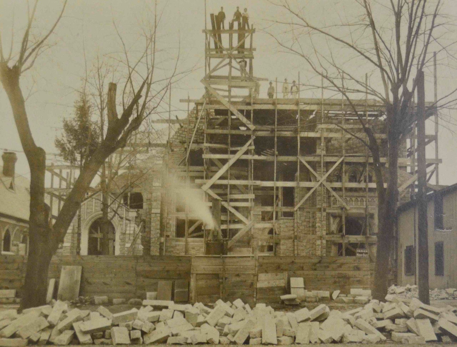 Old stone building under construction with scaffolding, bare trees, and rubble in the foreground