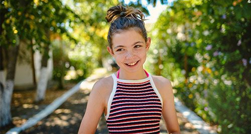 Smiling child in striped tank top standing on a sunny garden path