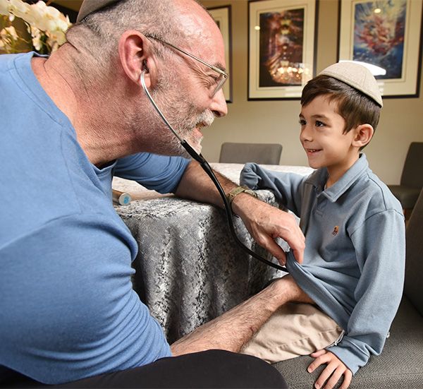 Dr. Michael Milobsky, pediatrician at Chicken Soup Concierge Pediatrics, listens to a boy's heart with a stethoscope