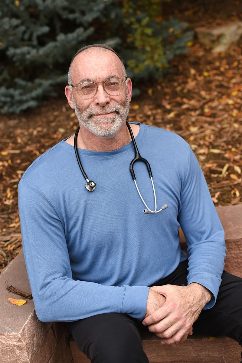 Man with stethoscope, blue shirt, sitting outside.