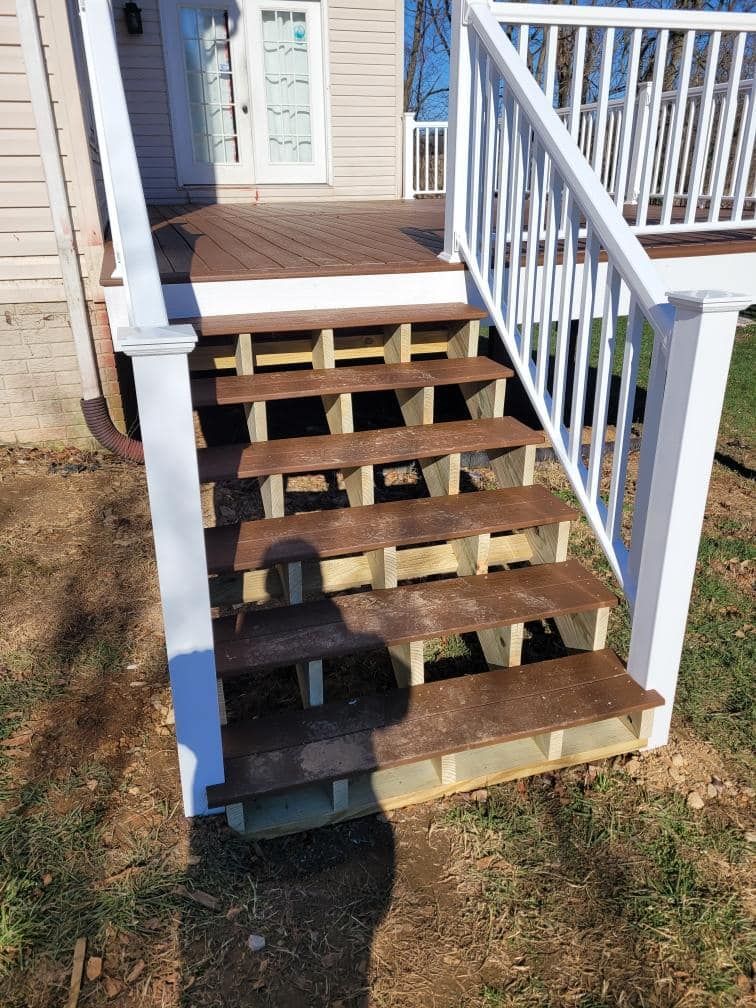 Deck stairs leading from a house to a yard, brown steps, white railing.