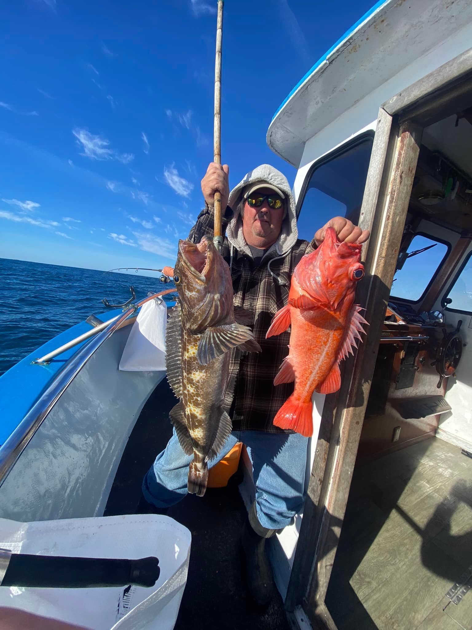 A man is sitting on a boat holding two fish.