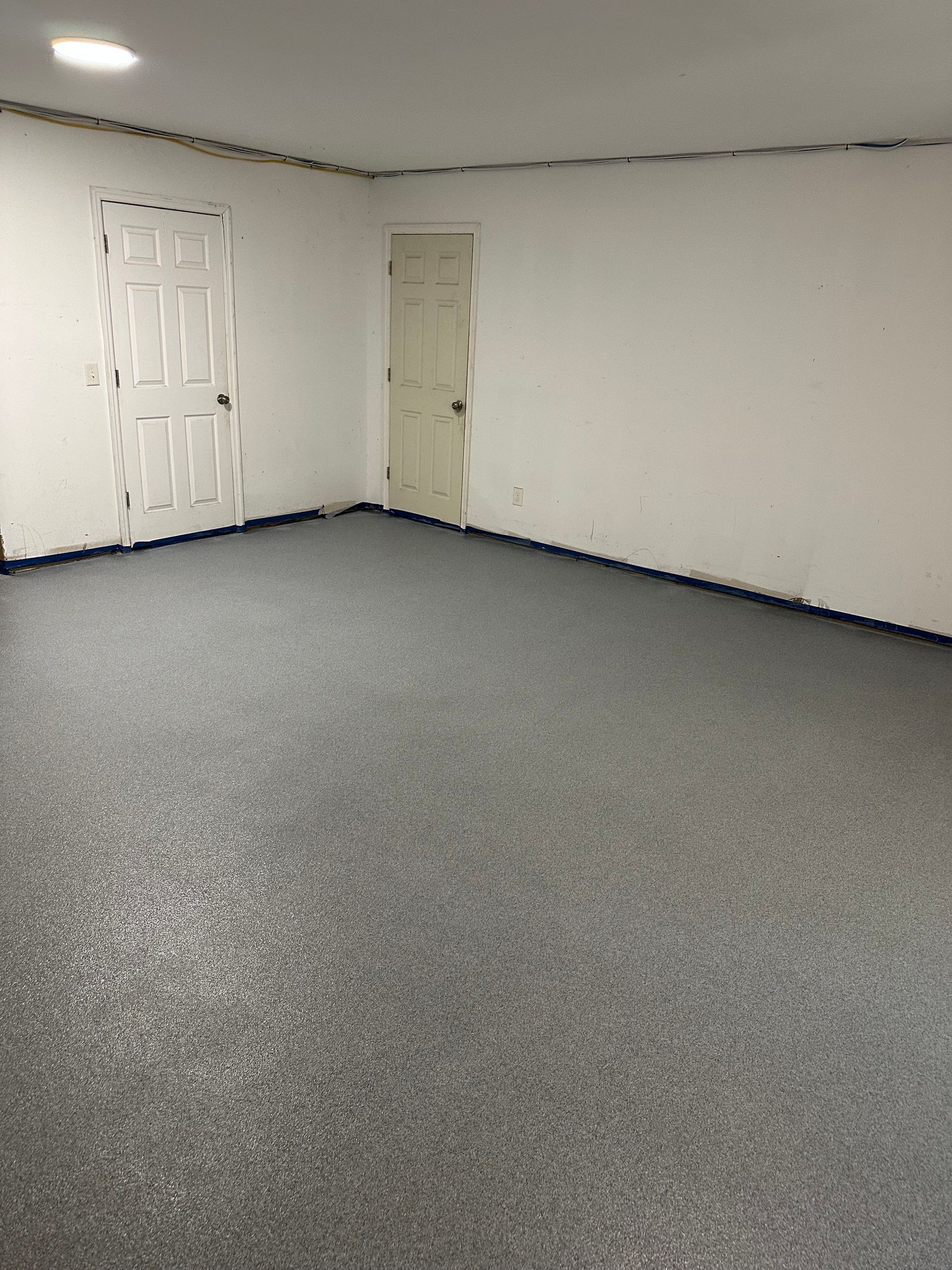 Empty carpeted room with white walls, two doors, and a low ceiling fixture.