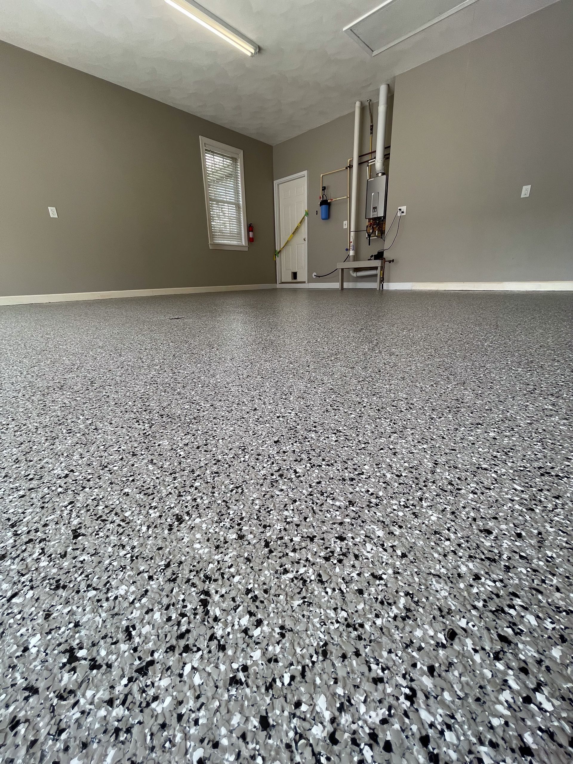 Empty garage interior with speckled epoxy floor and unfinished gray walls.