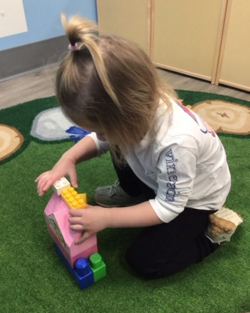 Girl playing with colorful building blocks on a green rug.