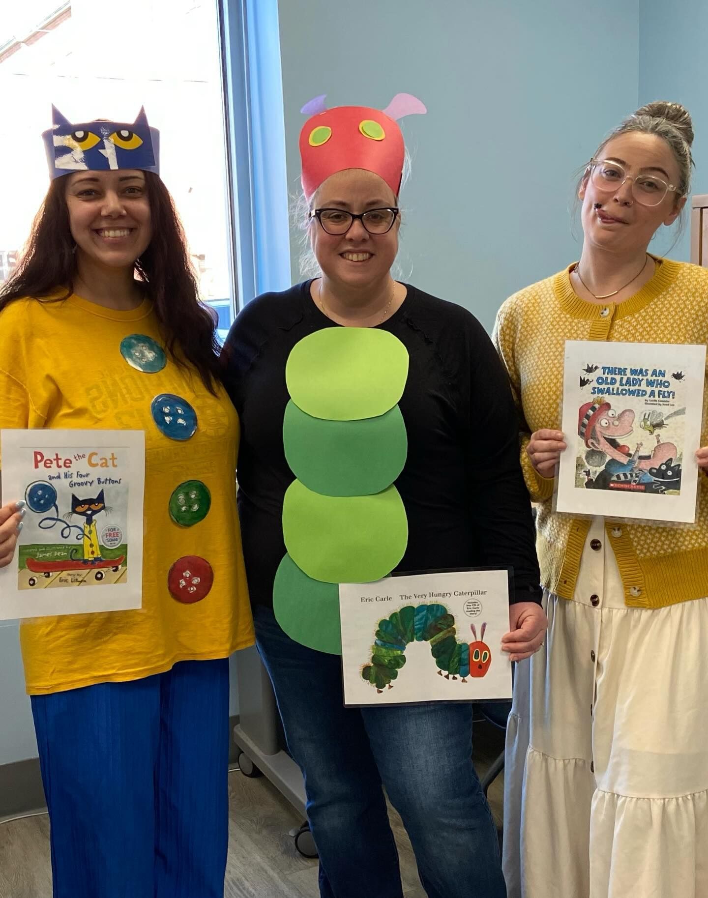 Three people dressed as book characters, holding related book covers, smiling.