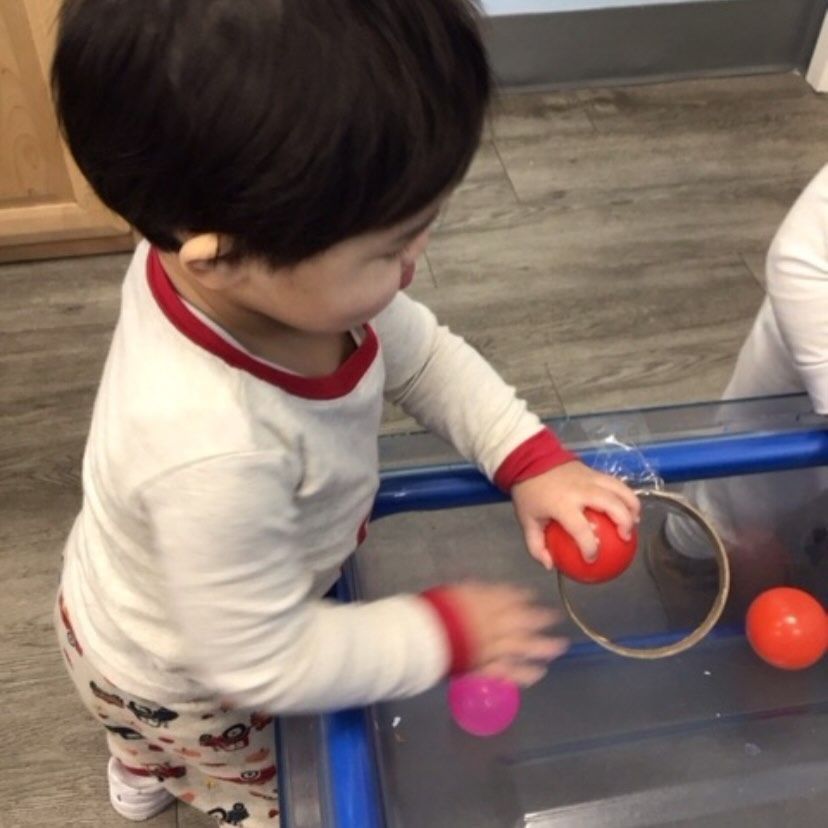 Young child playing with colorful balls near a plastic bin.
