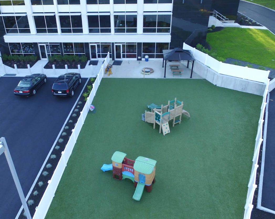Playground with a slide, near a tall building with many windows, and people gathering.
