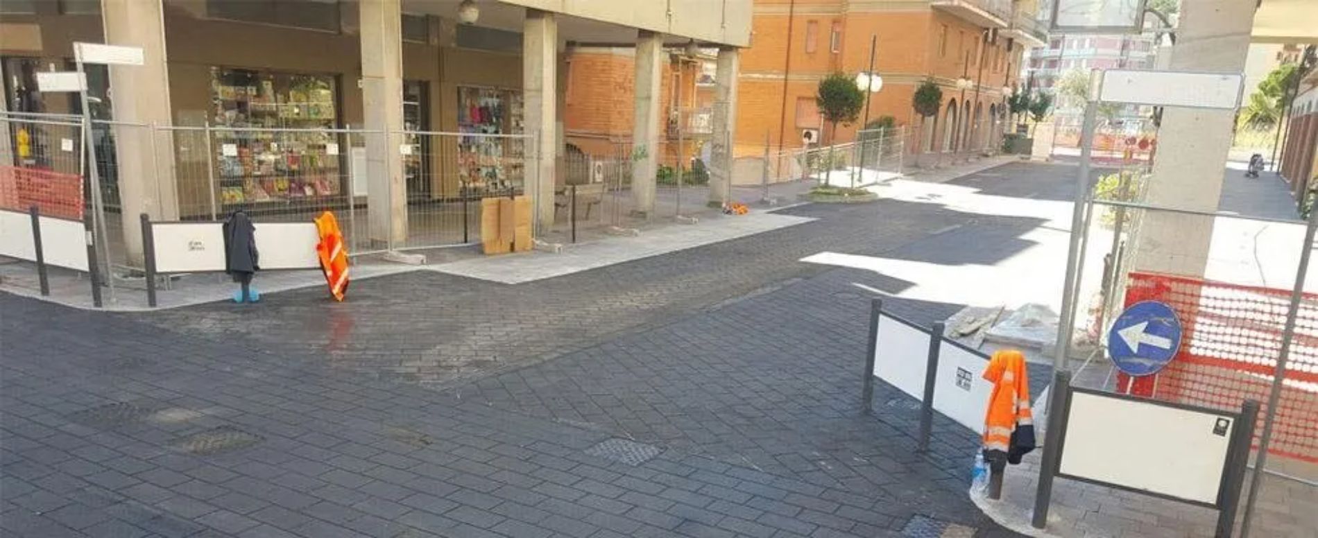 Scena di strada con operai vestiti di arancione e cartelli vicino a un edificio in mattoni.