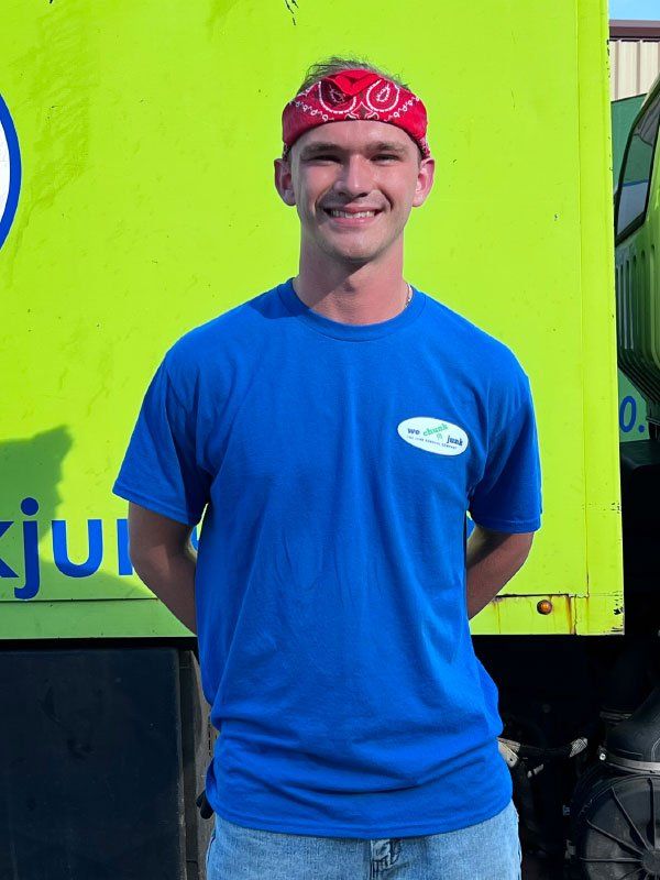 A man wearing a blue shirt and a red bandana stands in front of a green truck