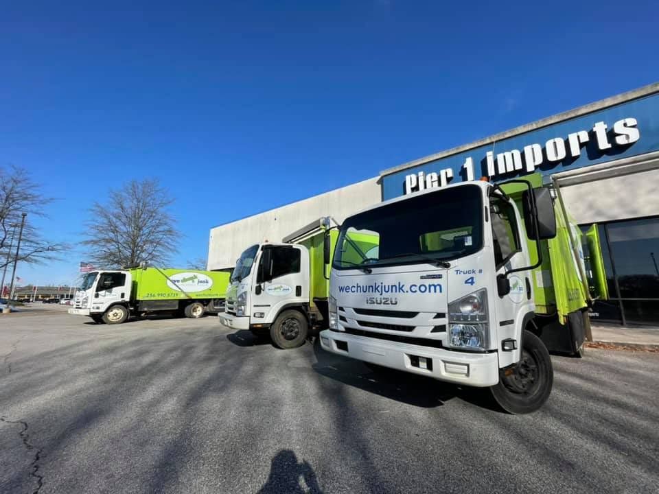 Three garbage trucks are parked in front of a building that says pier 1 imports.