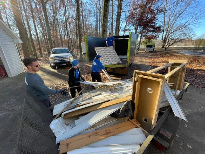 A group of people are loading a dumpster with junk on a trailer.