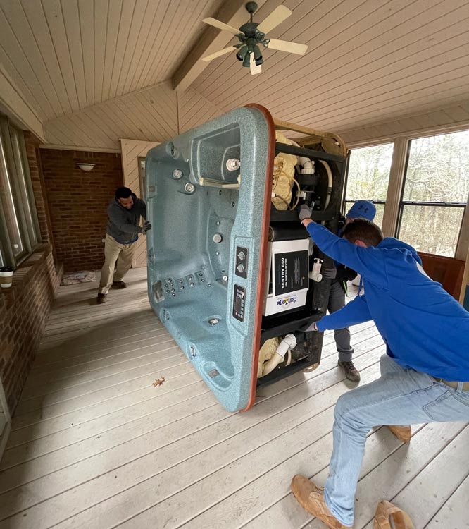 A man in a blue shirt is pushing a hot tub in a room.