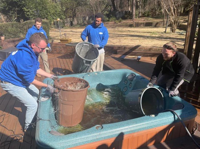 A group of men are cleaning a hot tub with buckets.