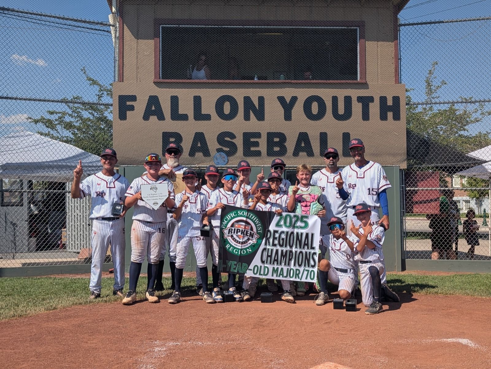Youth baseball team posing in front of a Fallon Youth Baseball sign, holding a championship banner.