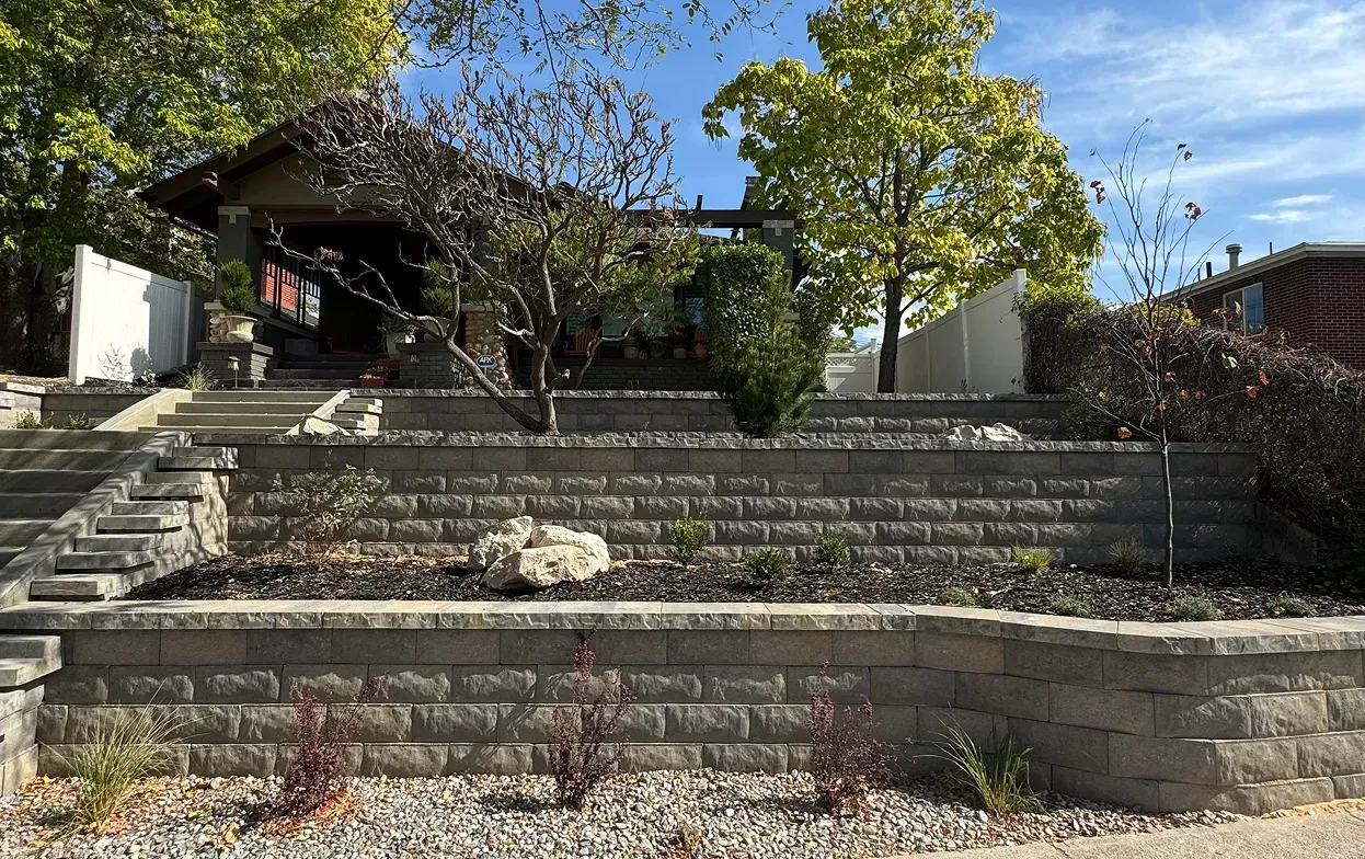 Stone patio with curved stone walls and built-in planters; wooden pergola in backyard.