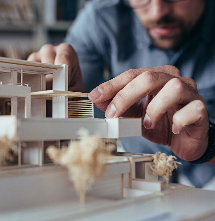 Architect adjusting a scale model of a modern building, focused hands, in a well-lit studio setting.