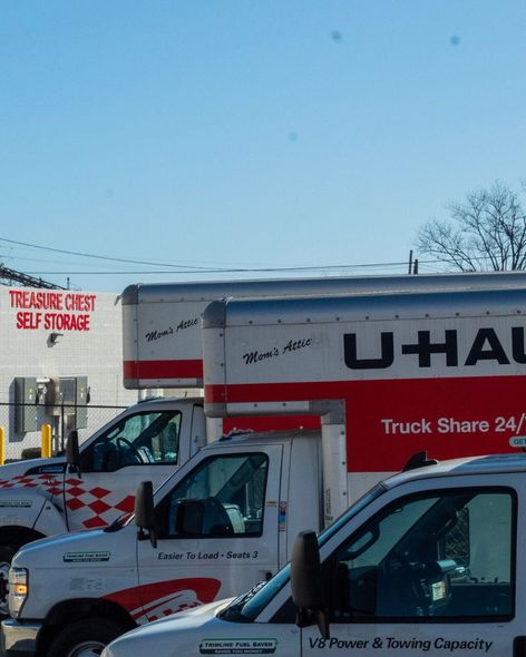 A line of parked white U-Haul moving trucks in front of a Treasure Chest Self Storage facility under a clear blue sky.