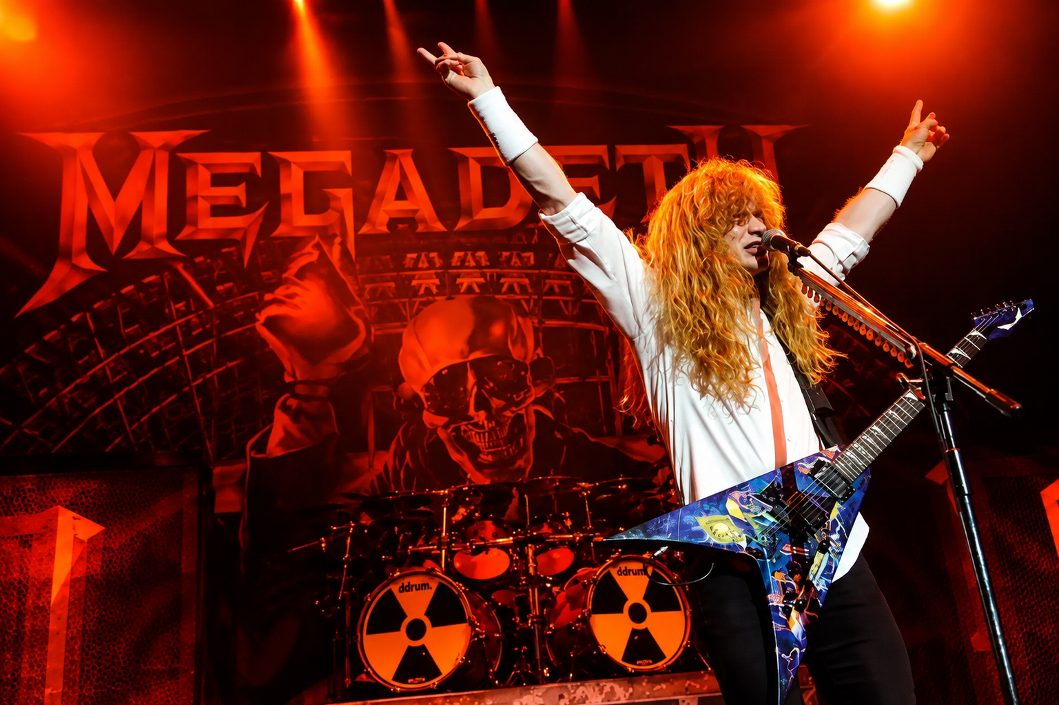Dave Mustaine celebrating with the crowd during Megadeth's farewell era. Dave Mustaine performs live with Megadeth, holding his Flying V guitar aloft beneath vivid purple stage lighting during the band's farewell era.