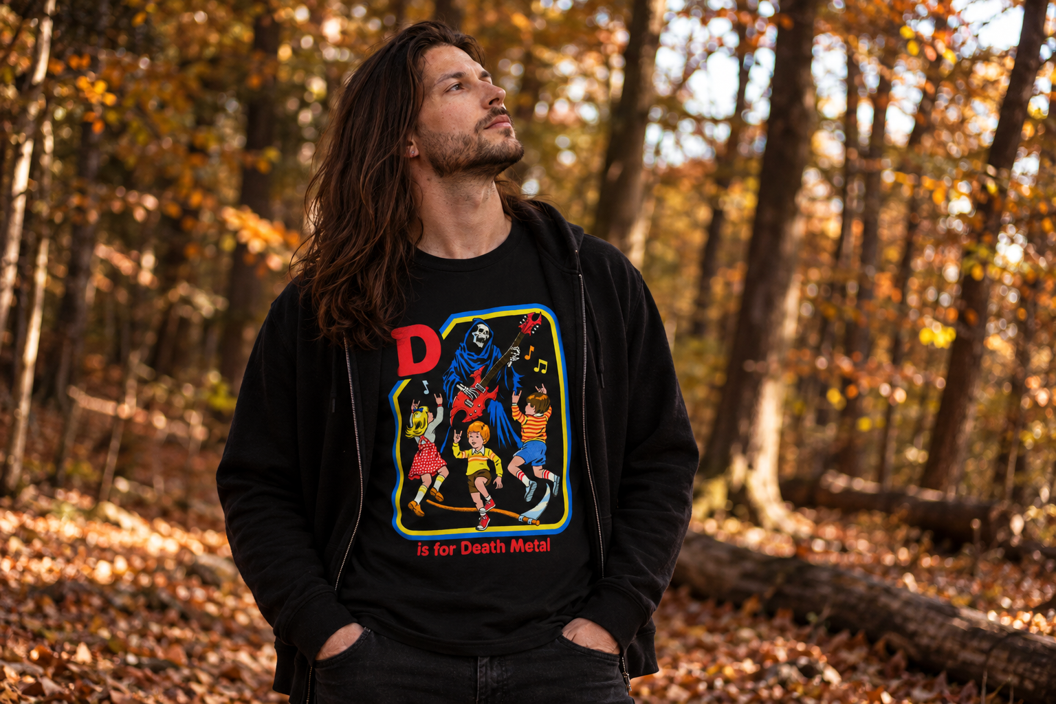 Long-haired man wearing a black D Is for Death Metal graphic T-shirt and black jacket in a sunlit autumn woodland.