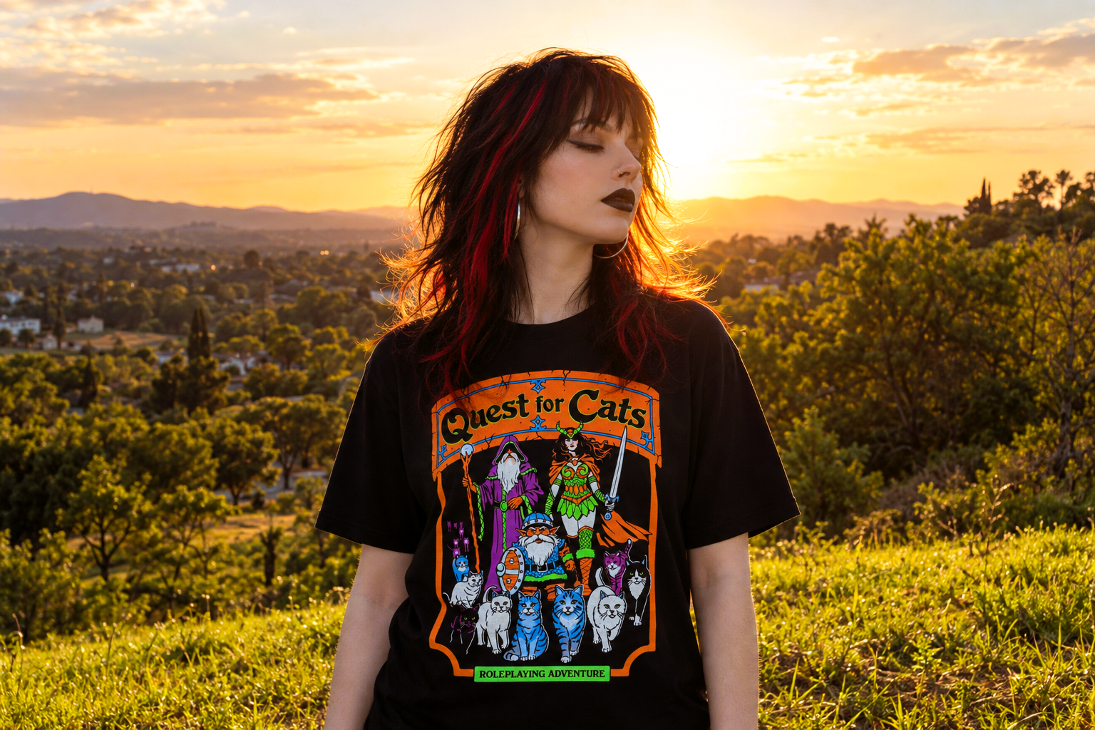 Woman wearing a black Quest for Cats graphic T-shirt outdoors at golden hour, with a sunlit countryside landscape behind her.