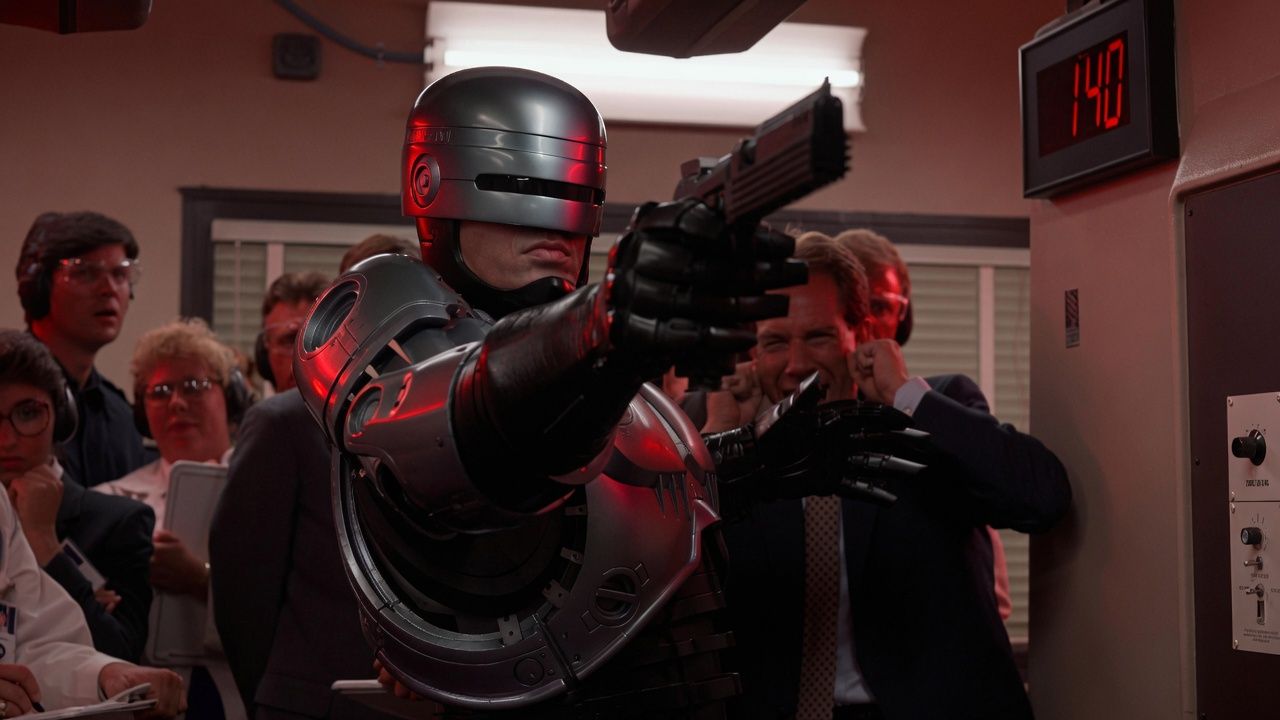 RoboCop confronts armed criminals in a scene from Paul Verhoeven's 1987 science fiction satire, illustrating the fusion of law enforcement and advanced technology.