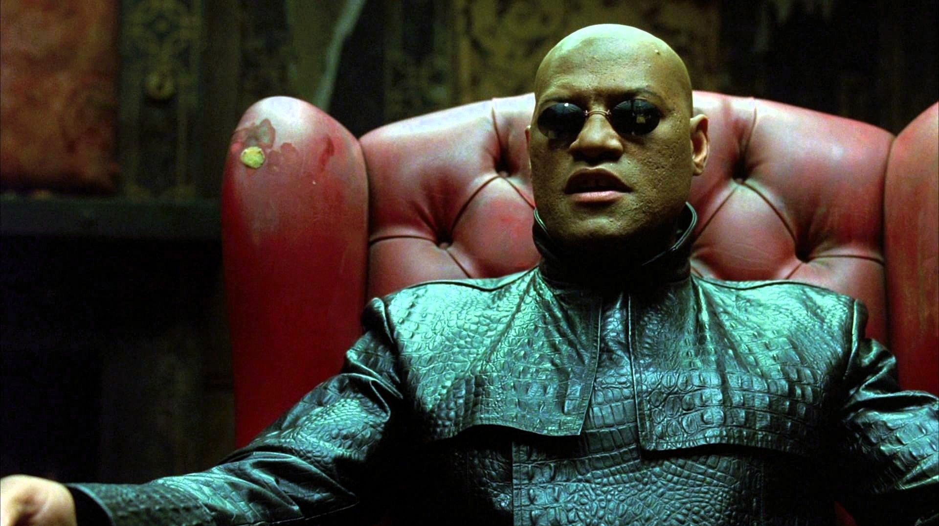Laurence Fishburne as Morpheus seated in the red leather chair during the iconic choice scene in The Matrix.