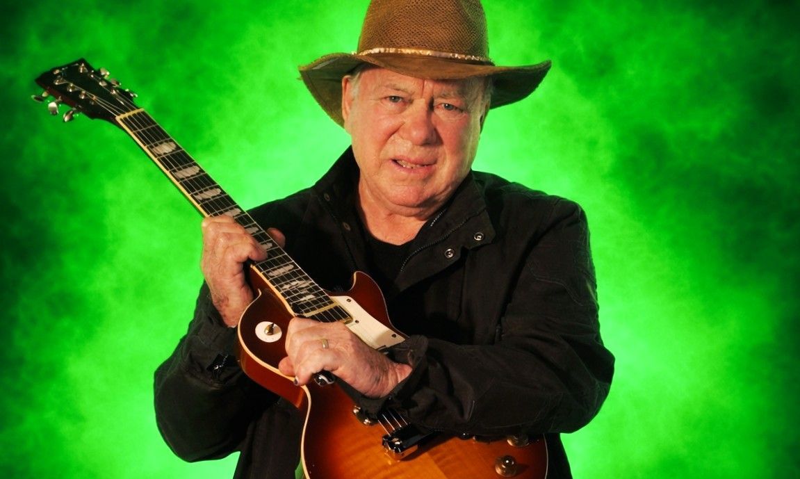 William Shatner holding an electric guitar during a promotional portrait reflecting his lifelong creative reinvention.
