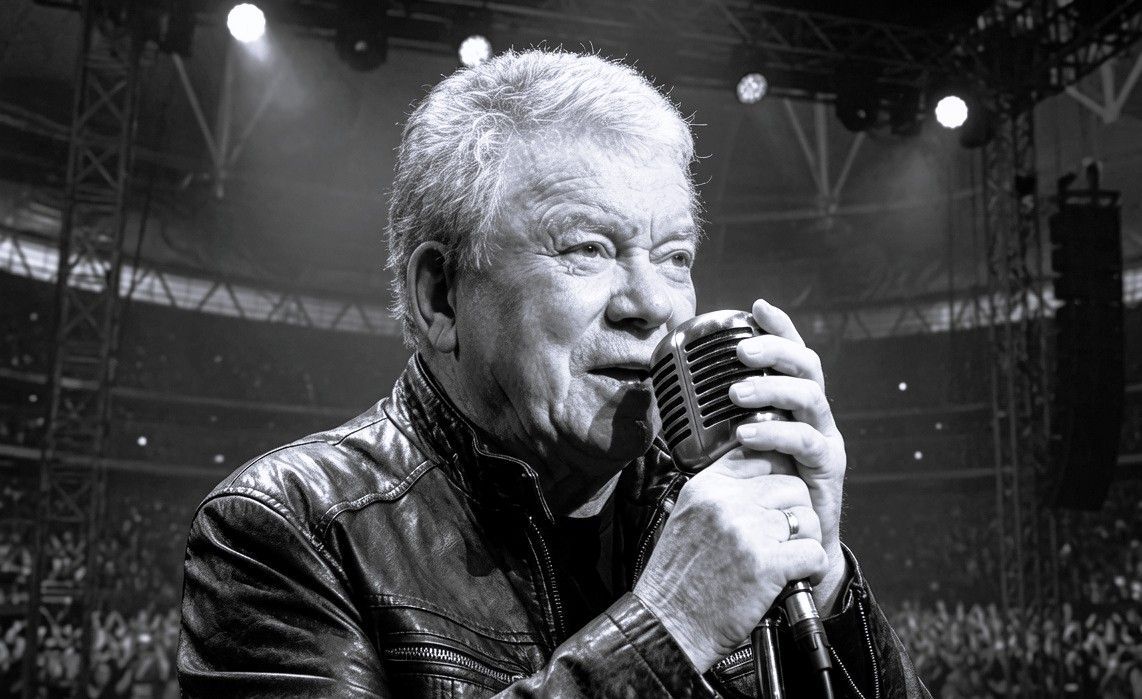 William Shatner performing with a vintage microphone during a conceptual heavy metal stage production.
