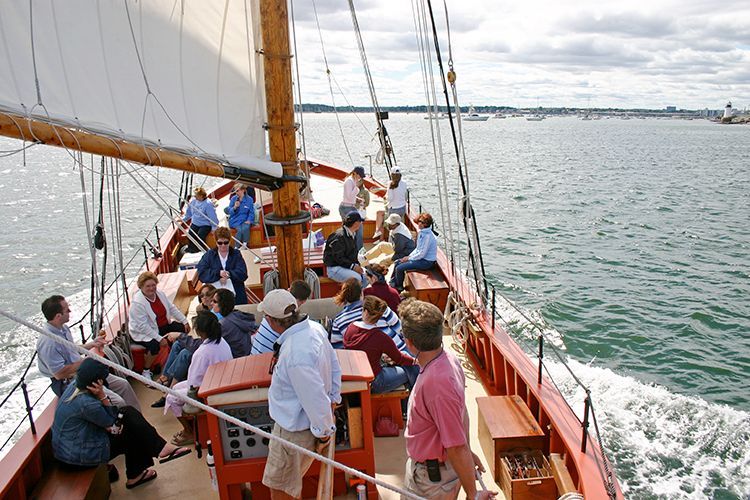 A group of people are sitting on the deck of a schooner in the Salem Harbor.