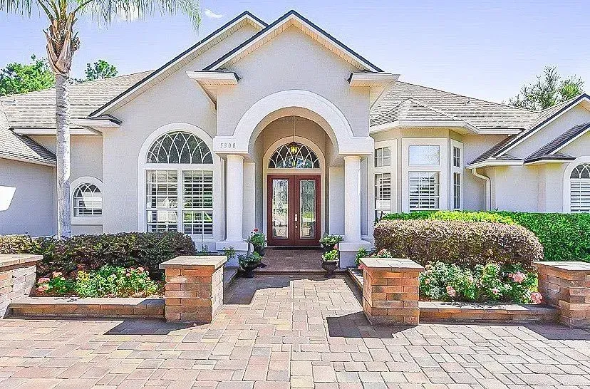 Elegant white stucco house with arched entry, brick walkway, and manicured front landscaping