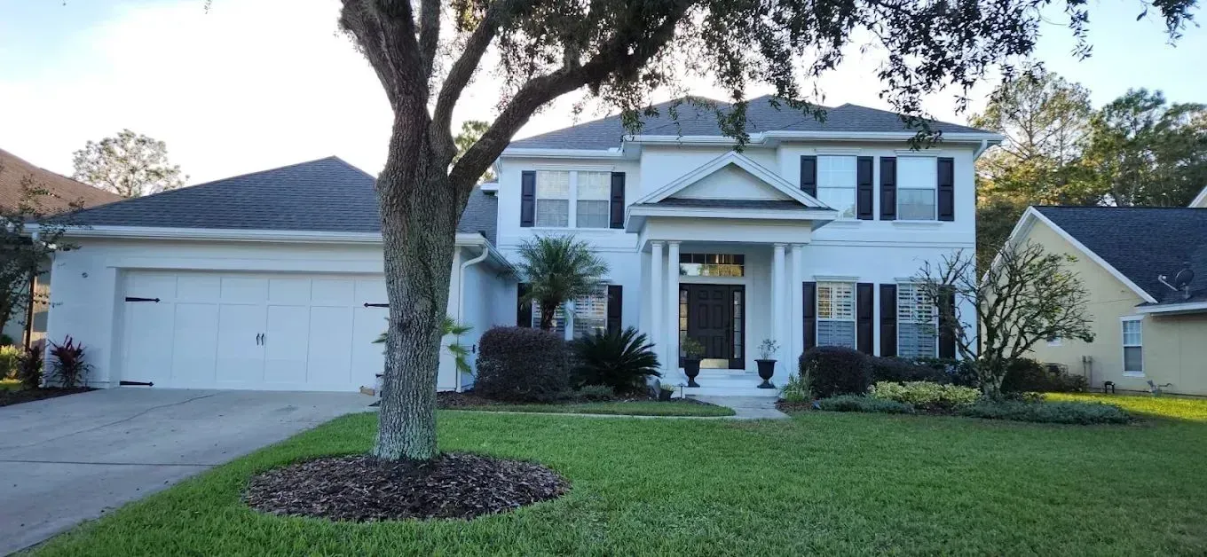 Two-story suburban house with white trim, a garage, and a large tree in the front yard