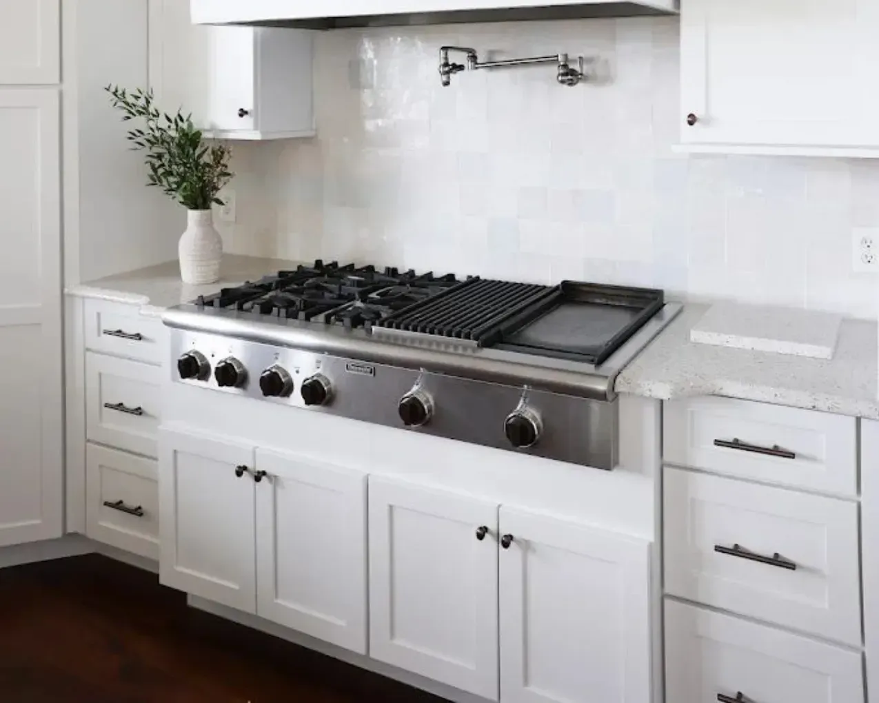 Modern white kitchen with stainless steel gas range and black cooktop under a white hood